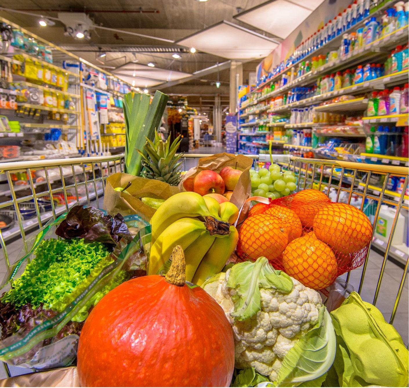 Einkaufswagen mit frischem Gemüse zwischen Regalen in einem Supermarkt