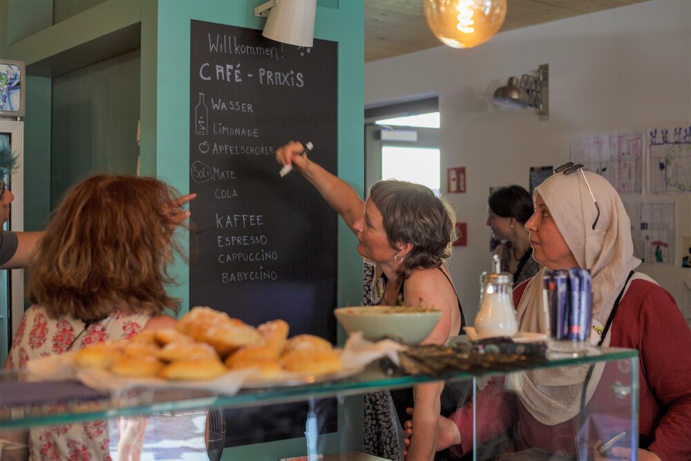 Das Foto zeigt Mitarbeitende der Café-Praxis, die auf eine Tafel schreiben